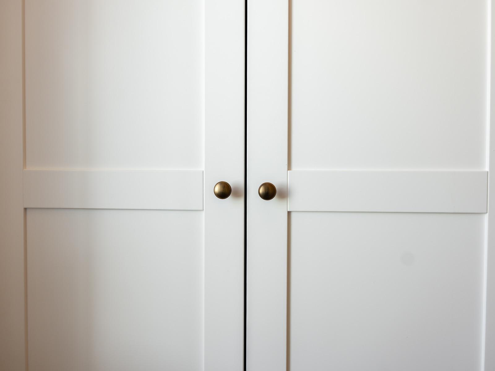 Close-up of white shaker-style wardrobe doors with antique brass round cabinet knobs