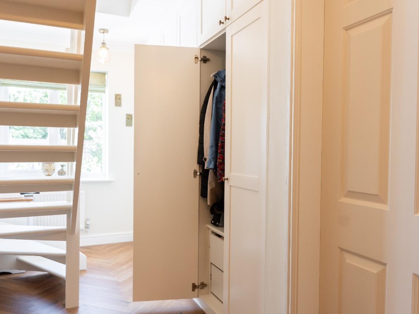 Open fitted wardrobe showing hanging rails, coats and drawers in a hallway dressing area