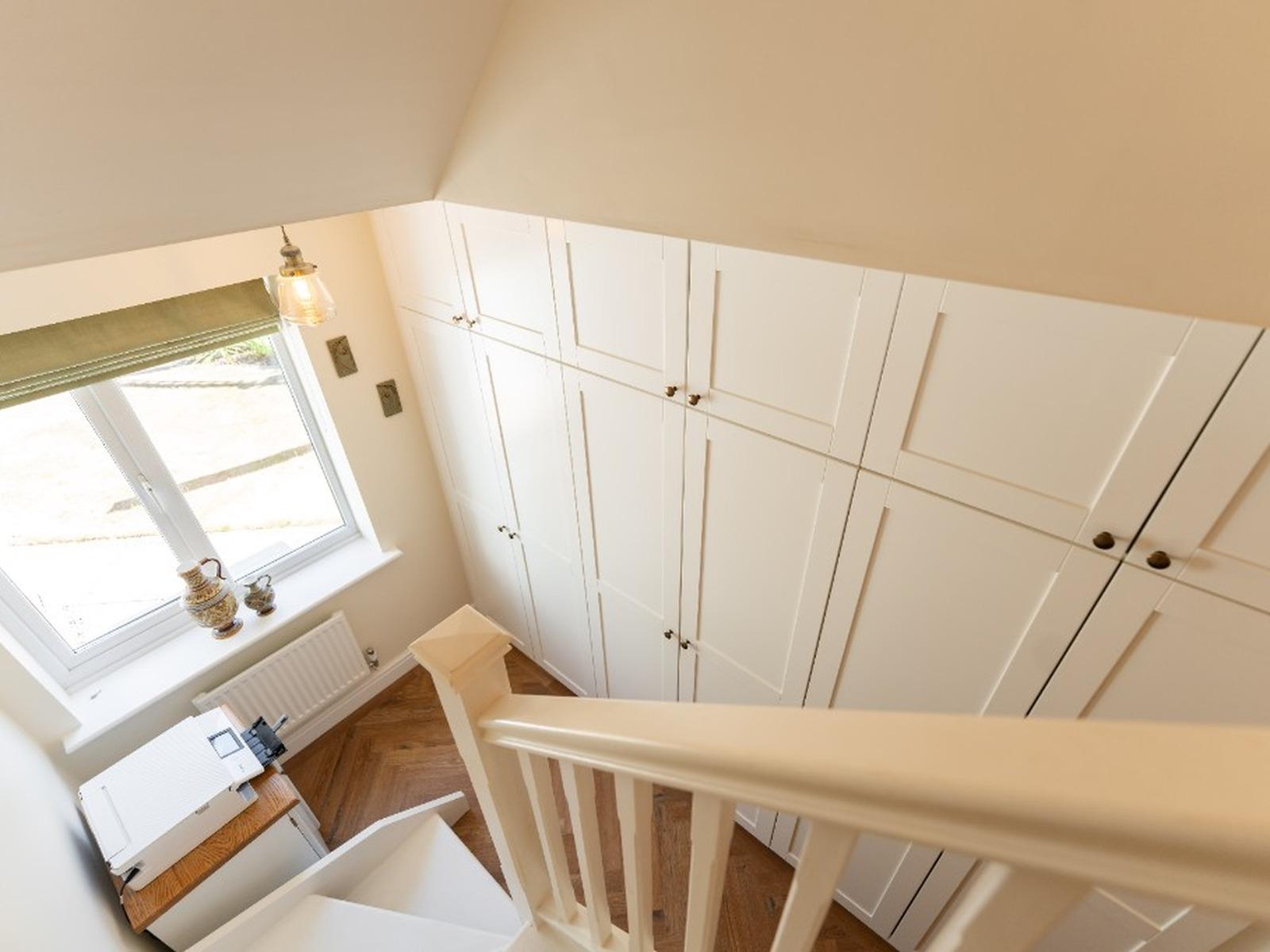 Floor-to-ceiling fitted wardrobes with top boxes following the ceiling line in a bright hallway