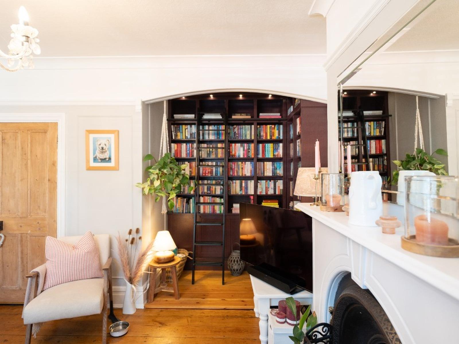 Floor-to-ceiling plum library fitted into a recessed alcove, with closed storage below and a sliding ladder