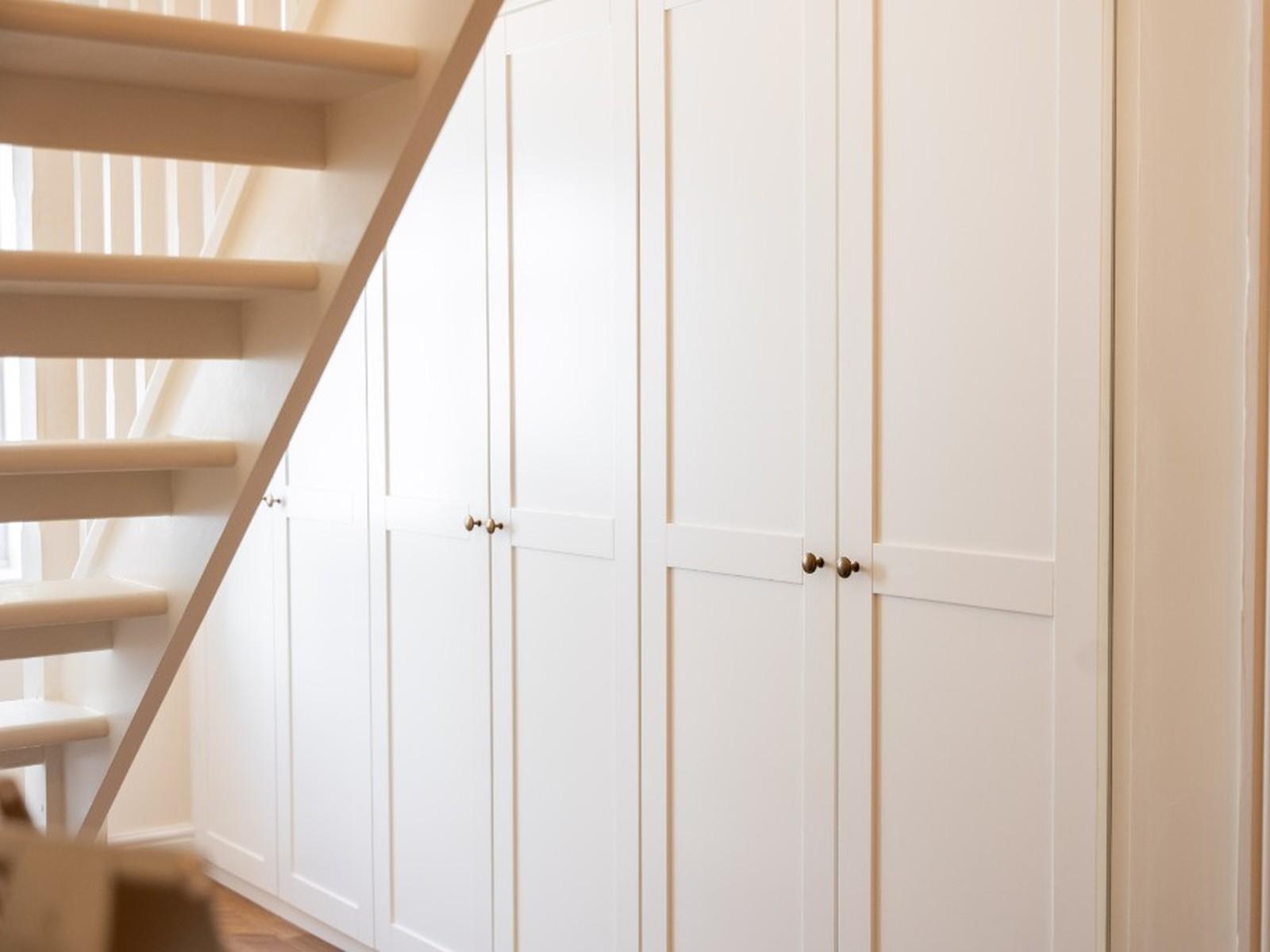 Cream Shaker-style fitted wardrobes built under a staircase, with brass knobs